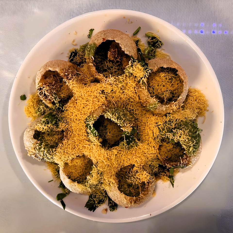 A plate of Indian pani puri, filled with green chutney and topped with yellow sev.