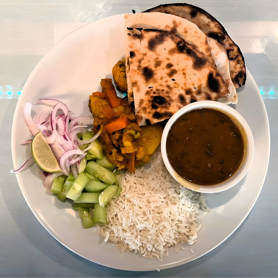 A white plate with Indian food including naan, rice, curry, dal, and a cucumber and onion salad.
