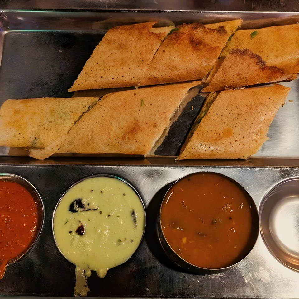 Crispy golden dosas, cut into triangles, served with three bowls of colorful chutneys on a metal tray.