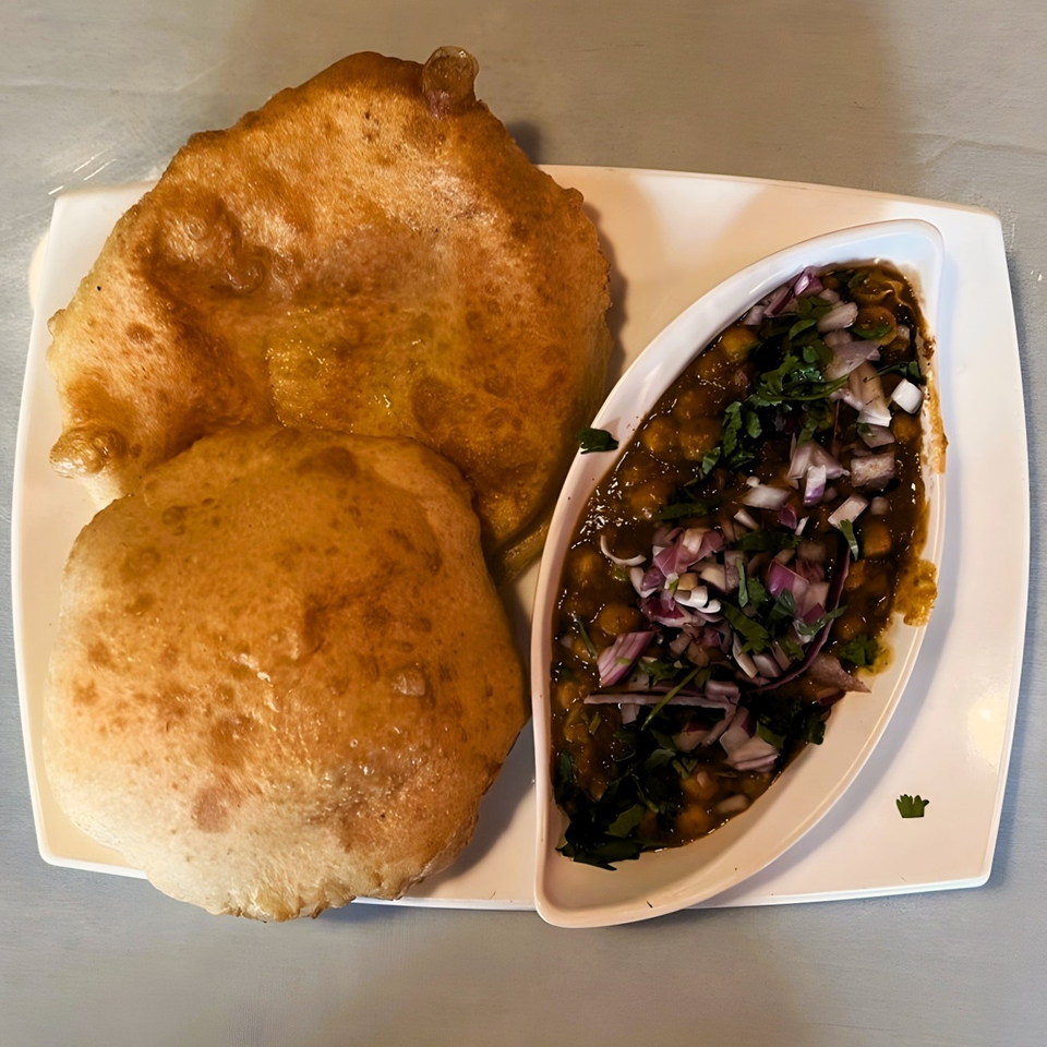 Two golden-brown fried breads (bhature) served with a bowl of chana masala, topped with red onions and cilantro.