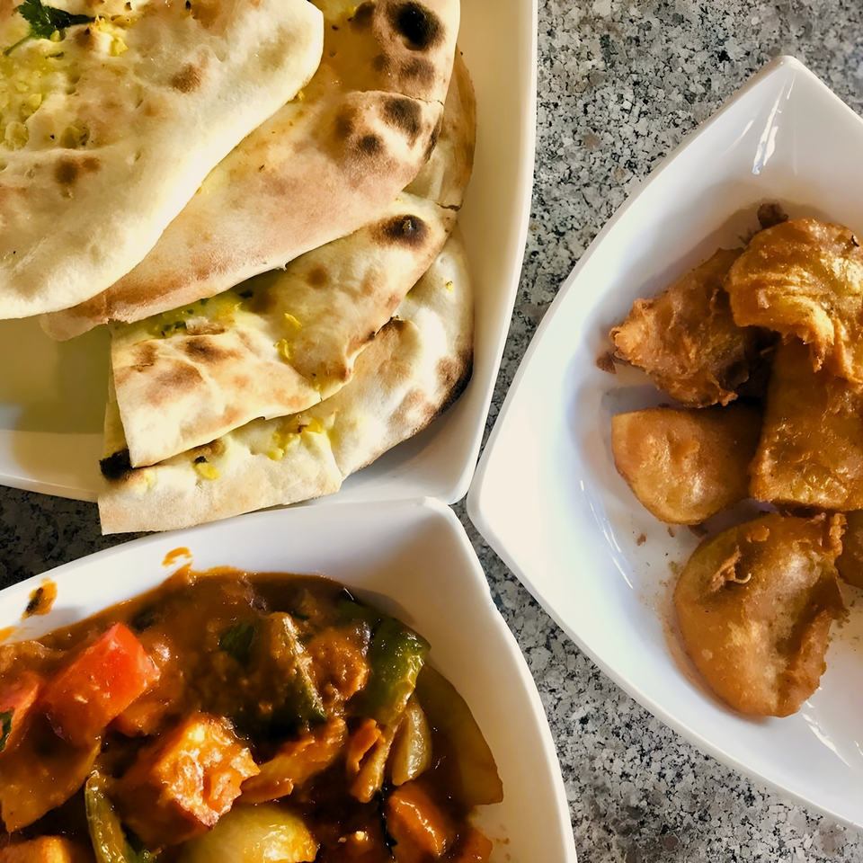 Indian dishes including naan bread, fried pakoras, and a vegetable curry on a granite table.